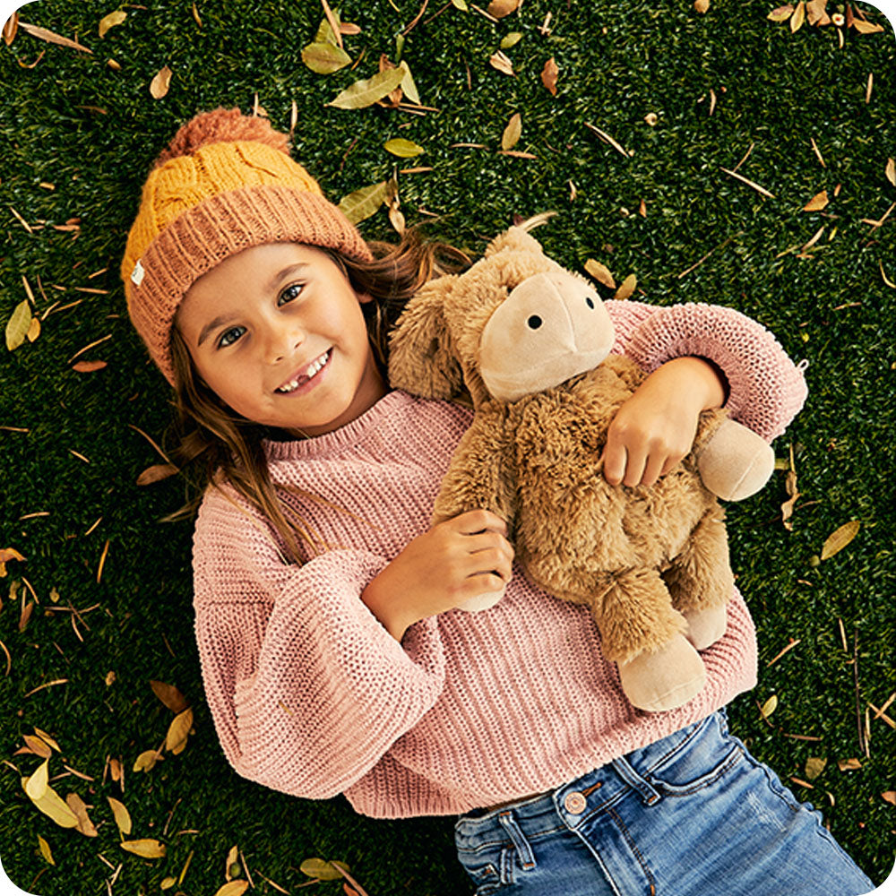 Image 102: girl wearing sweater holding warmies donkey stuffed animal