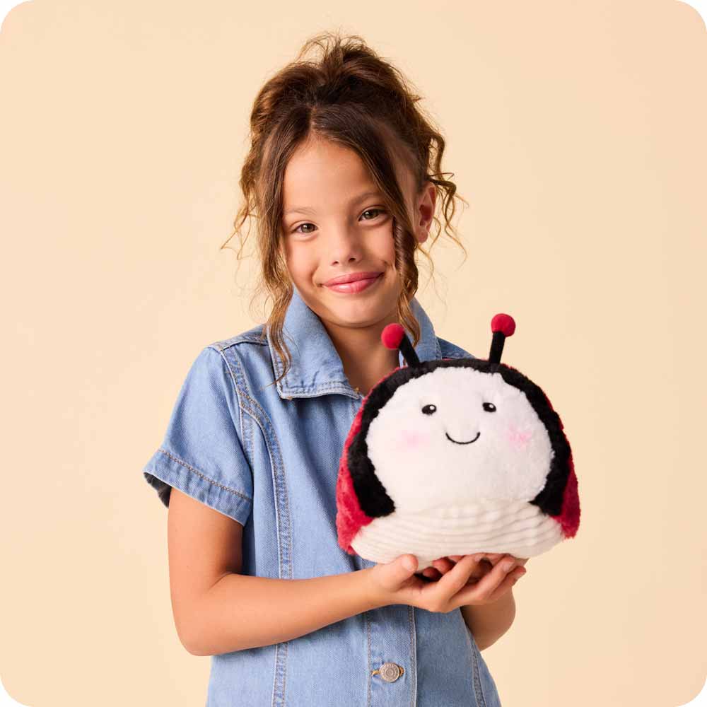 Image 103: Ladybug Warmies being held by a little girl in a blue dress against a yellow background