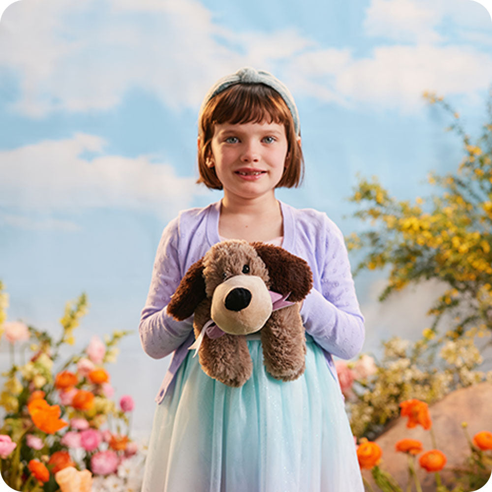 Image 101: girl holding a brown dog stuffed animal in a flower field